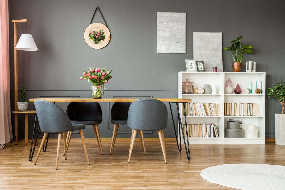 White wooden rack with books, decor and fresh plants standing in grey dining room interior